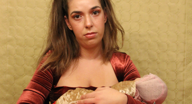 Een vrouw in een rode top houdt een baby-pop vast aan een kersttafel.