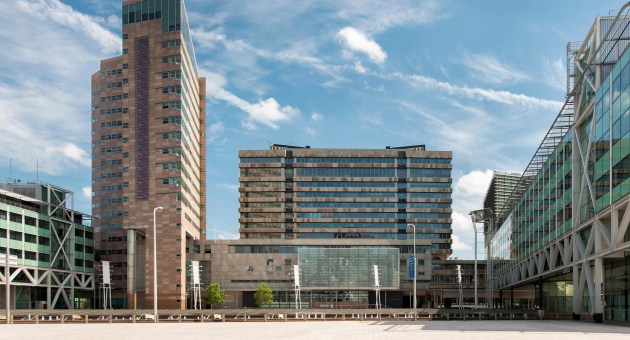 Drie moderne kantoorgebouwen met glazen gevels onder een blauwe lucht.