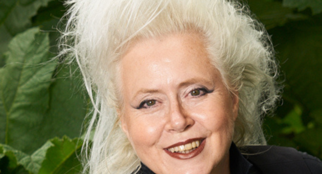 Een vrouw met lang, wit haar en een zwarte outfit glimlacht.