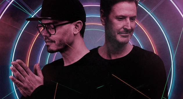 Twee mannen poseren voor een kleurrijke neon achtergrond.