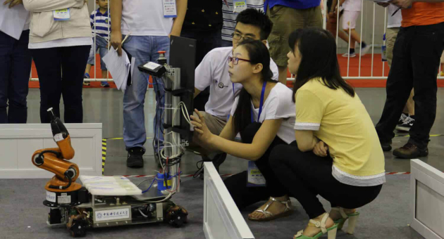 Groep mensen volgt een robotdemonstratie met een robotarm.