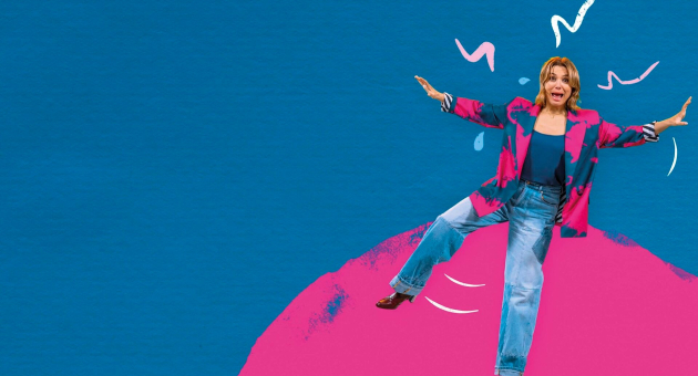 Vrouw in een kleurrijke blazer en spijkerbroek op een roze achtergrond.