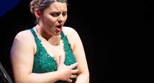 Een vrouw in een groene jurk zingt emotioneel op een podium.