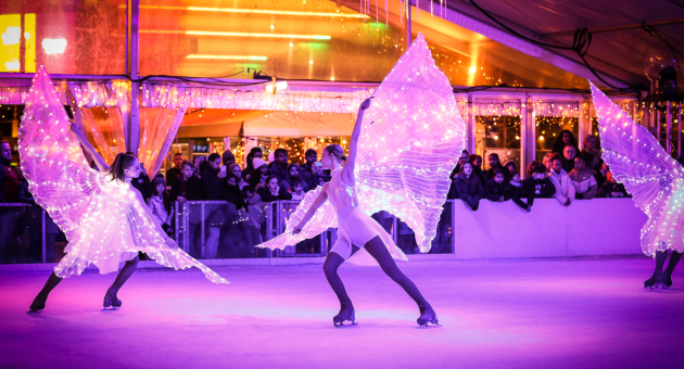 Twee vrouwelijke schaatser zwierend op het ijs in witte pakjes met verlichte vleugels.