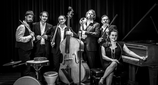 Zeven muzikanten poseren met instrumenten in zwart-wit.