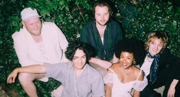 Vijf bandleden van Future Husband poseren samen op een bankje omringd door groen.