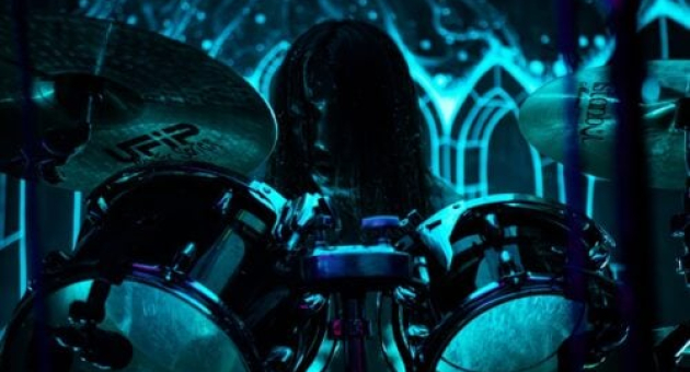 Drummer met lange haren achter een drumstel, verlicht door blauwe lichten.