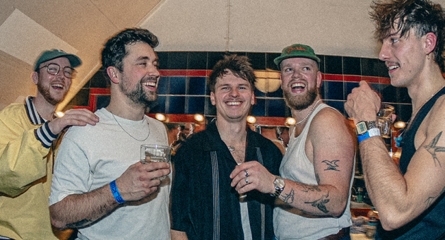 Vijf lachende vrienden met drank in hun handen, gekleed in casual kleding.