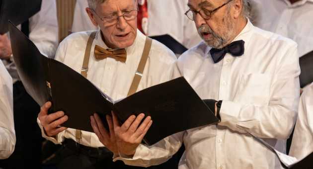 Twee mannen in witte overhemden en vlinderstrik lezen een koorboek.