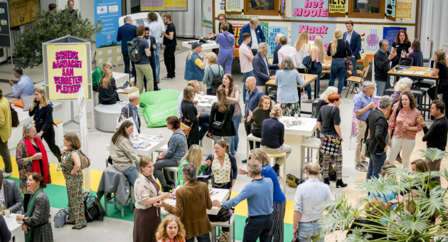 Drukke netwerksessie met mensen in gesprek aan tafels tijdens een evenement in een creatieve, informele setting.