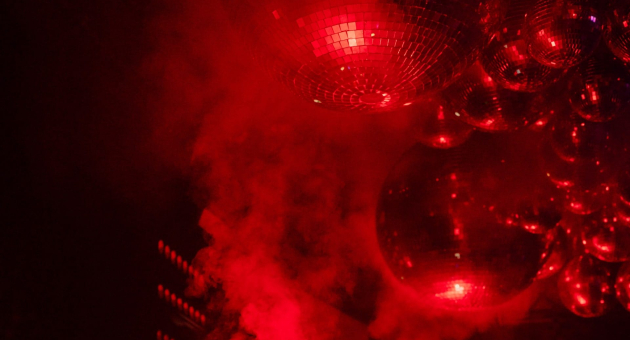 Disco balls hang above a lit dance floor in red light
