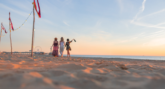 Drie vrouwen wandelen over het strand bij zonsondergang.