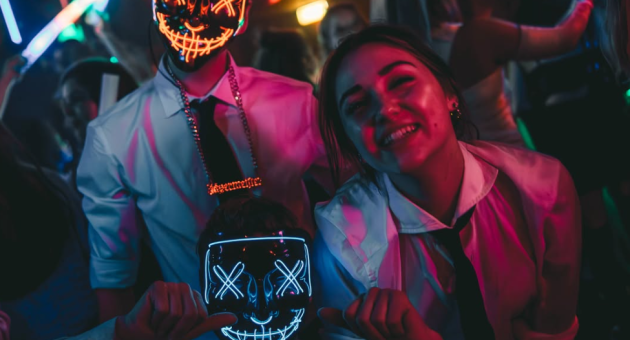 Drie jongeren met lichtgevende maskers op een feest.