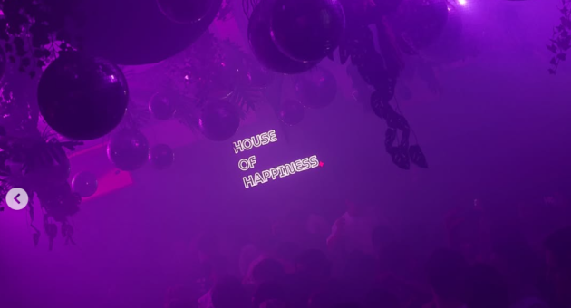 Een drukke feestzaal met paarse verlichting en discoballen. (c) House of Happiness