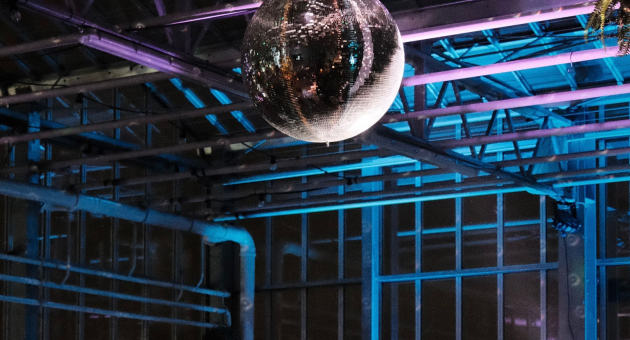 Een drukke dansvloer verlicht door een spiegelbal en gekleurd licht.