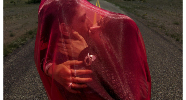 Een stelletje kust elkaar, bedekt met een rood doek, op een weg. Inez & Vinoodh, Think love, 2025