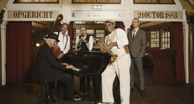 Vijf muzikanten spelen jazz in een café met een piano.