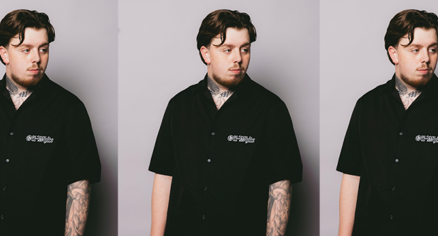 Portret van Rotterdamse rapper Jack in zwart overhemd opzij kijkend.