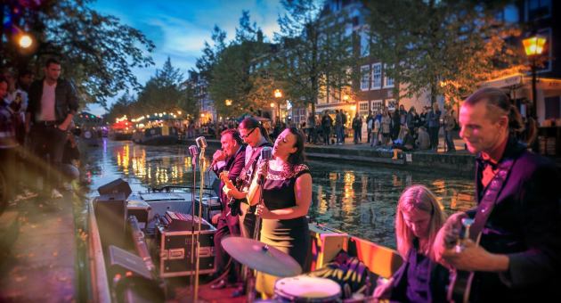 4 muzikanten en een zangeres treden op in een bootje tijdens festival Jazz in de Gracht aan de Bierkade. Aan de kades staan mensen te luisteren