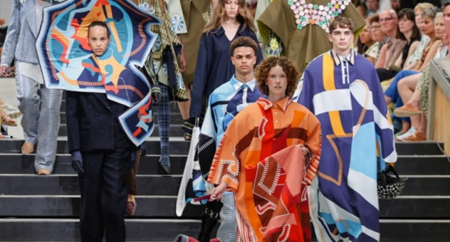 Fashion show featuring diverse outfits. Models walking a runway in striking clothing with prints and colors.