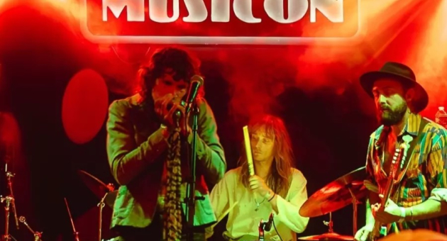 Een band speelt op het podium bij MusicOn, met gekleurde lichten.