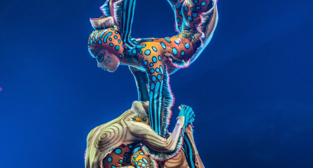 Drie acrobaten in kleurrijke kostuums vormen een kunstwerk.