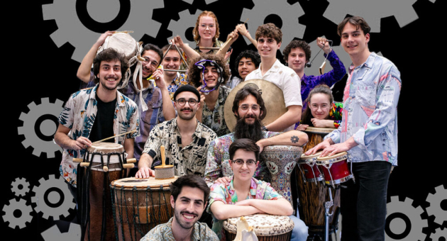 De leden van La Maquina poseren voor de camera in kleurrijke kleding met hun percussie-instrumenten. De groep straalt energie, diversiteit en eenheid uit, klaar voor een ritmisch avontuur.