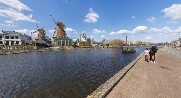 Een jongen leidt een paard langs een molen aan het water.