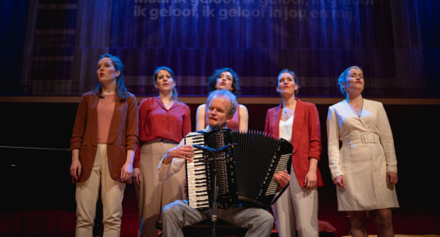 Een man met een accordeon speelt terwijl vijf vrouwen zingen op een podium.