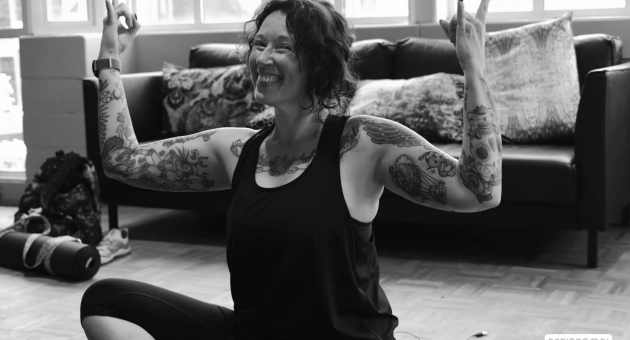 Vrouw met tatoeages in yogapose. Vrouw met korte haren en tatoeages, zittend met twee vingers omhoog.