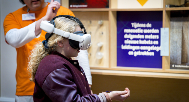 Een meisje met een VR-bril ervaart virtual reality terwijl een begeleider uitlegt.
