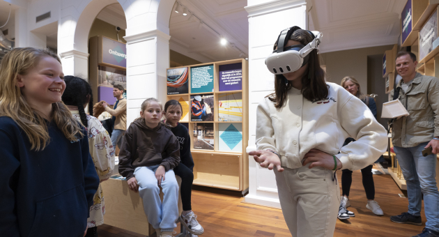 Een kind met een VR-bril, omringd door lachende vrienden.