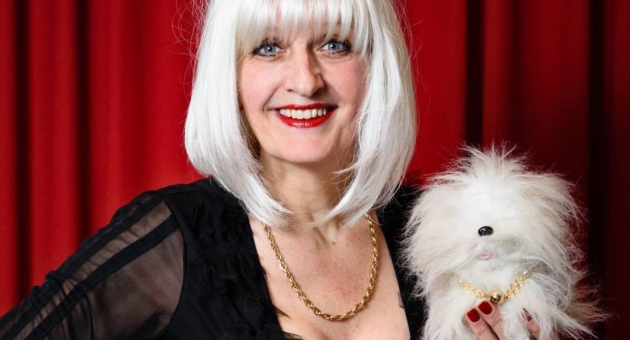 Vrouw met lange witte haren en een faux hondje in haar hand.