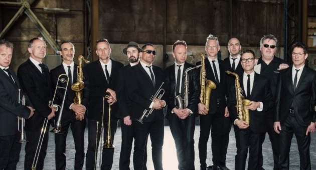 New Cool Collective Big Band in nette zwarte pakken met stropdas poseert voor de lens met hun instrumenten.