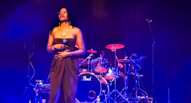 Een vrouw in een lange jurk zingt op het podium met een band achter haar.