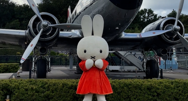 Miffy in een rode jurk staat voor een vliegtuig.