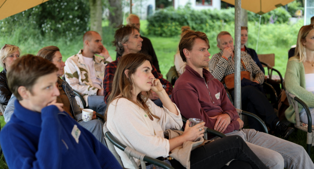 Groep mensen zit onder een parasol en luistert aandachtig.