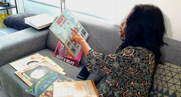 Een vrouw zit op een bank en wijst naar een platenhoes.