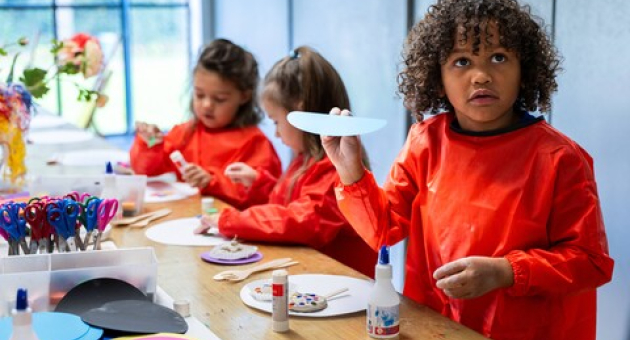 Kinderen in oranje schorten knutselen met papier en lijm.