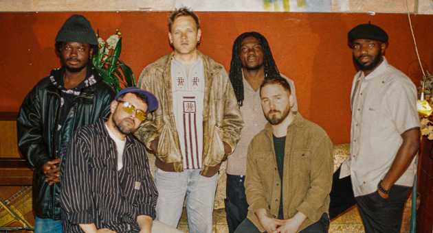 Zes mensen poseren in een café met een warme sfeer.