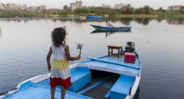 A girl holding a flower stands on a blue boat.