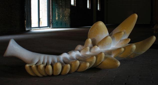 Gele en witte sculptuur met golvende vormen in een donkere ruimte