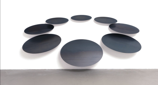 Zwarte, ovale kunstpanelen hangen aan een witte muur.