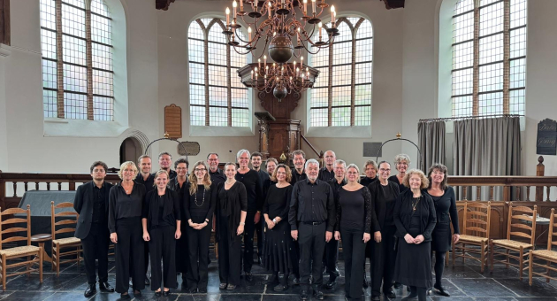 Een koorgroep in zwarte kleding poseert binnen.