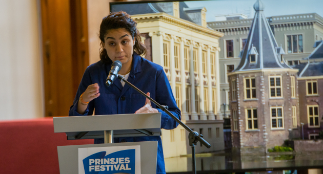 Een vrouw staat achter een microfoon en spreekt.