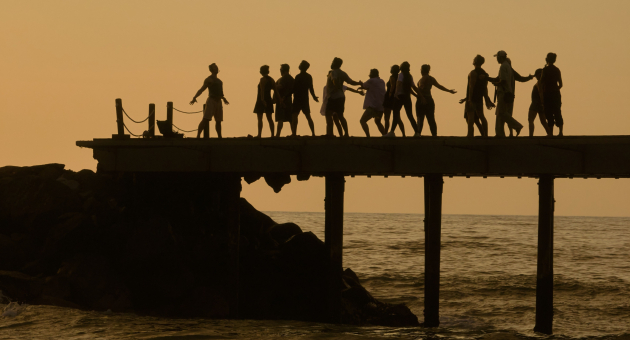Silhouetten van mensen die op een pier dansen bij zonsondergang