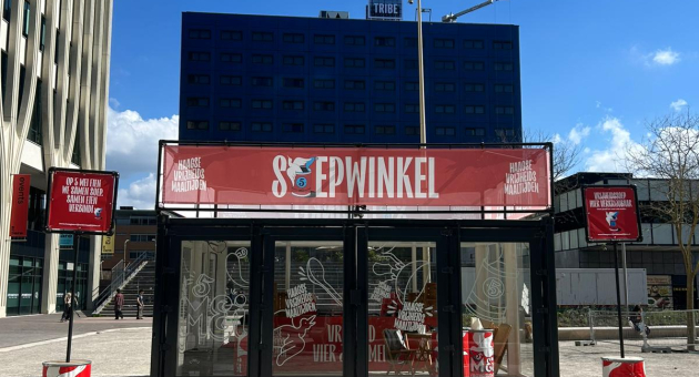 Een glazen container met een rode banner van Soepwinkel en een blauwe lucht