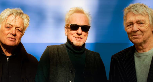 Drie mannen poseren met zonnebrillen tegen een blauwe achtergrond.