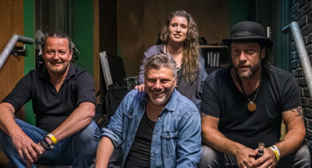 De band zit lachend op een trap, klaar voor hun optreden.