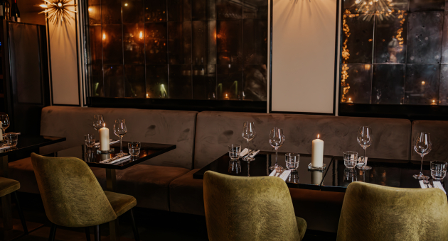 Gedekte tafels met kaarslicht, fluwelen stoelen en spiegelwanden in een sfeervol restaurantinterieur